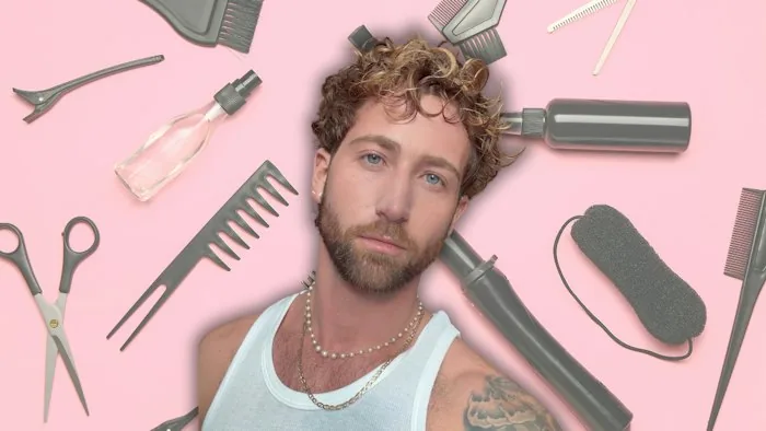 Zachary Travers in front of a pink backdrop with hair tools.